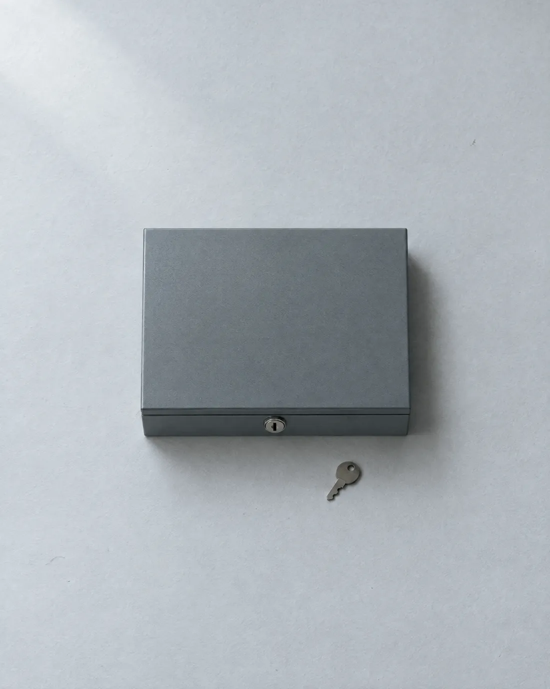 A closed grey steel document box with its key beside it.