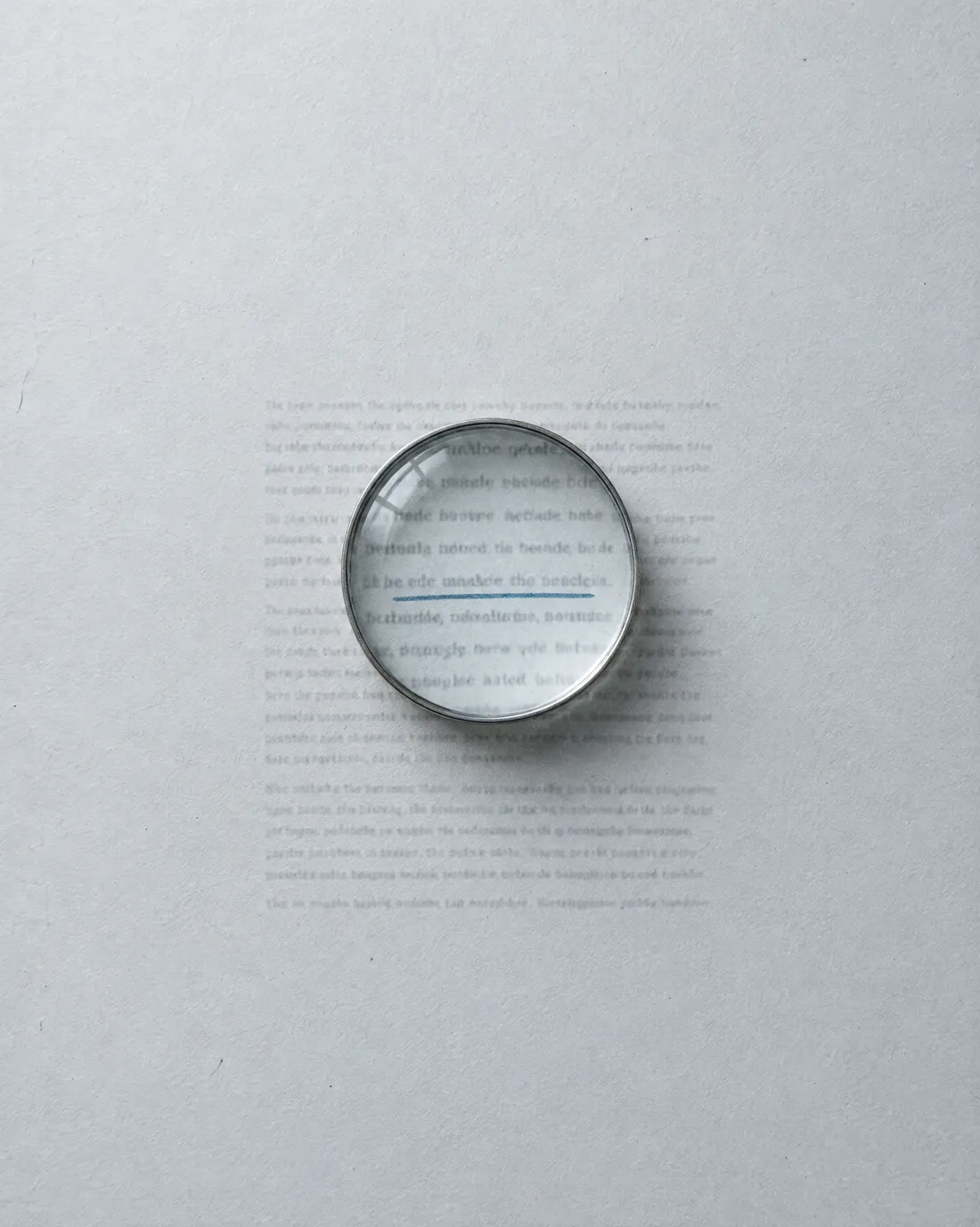 A magnifying loupe on a printed page, one line underlined in blue.