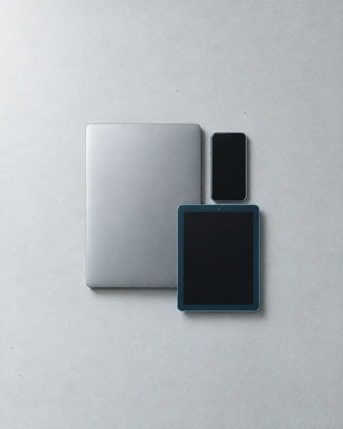 A closed laptop, a phone and a tablet laid out neatly.