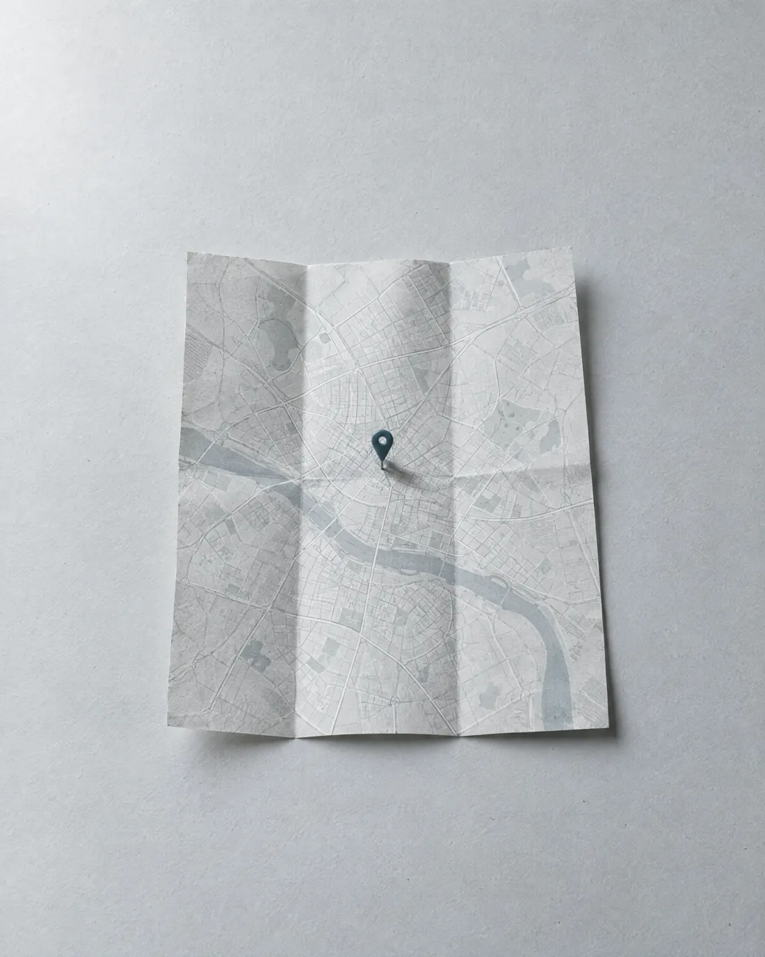A folded city map with one blue pin pushed into it.